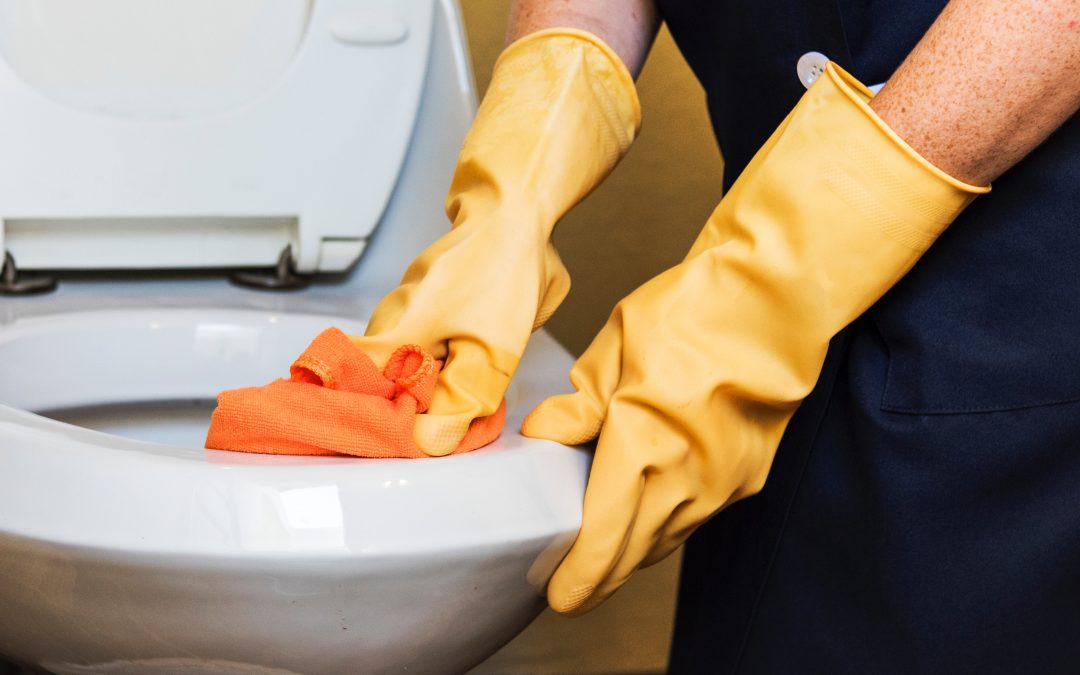 A person with heavy-duty yellow gloves scrubs a toilet bowl.