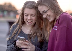 Two young, female college students laugh at something they see on a smartphone.